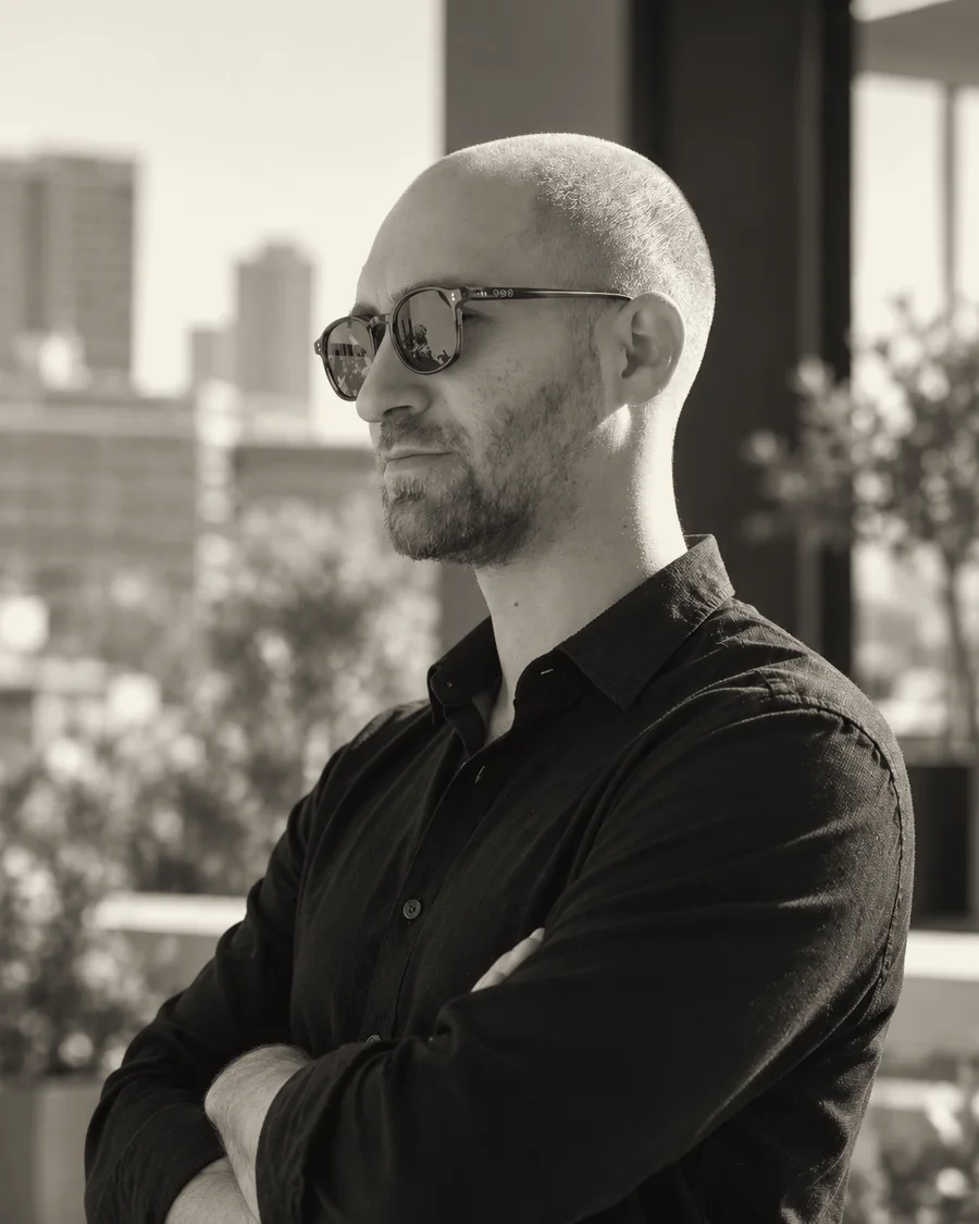 Benny, partner at Art-E-Shock, in a black shirt and sunglasses on a terrace facing the skyline